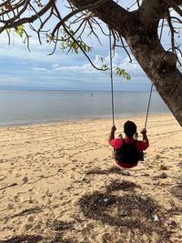 Scenic view of sea against sky with a man on a swing