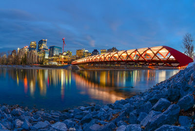 Illuminated city by river against sky at night