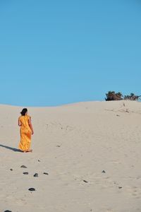 Rear view of woman on desert against clear sky