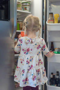 Rear view of girl standing by refrigerator