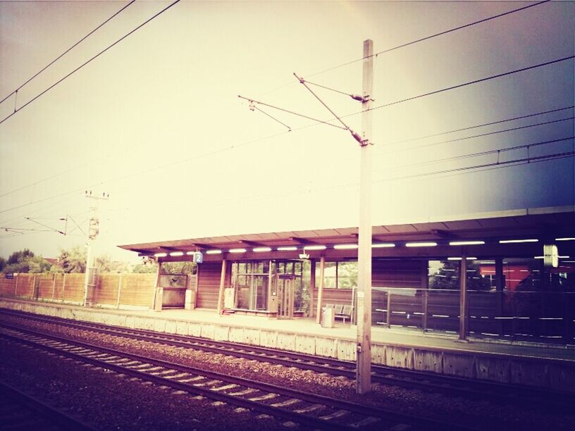 railroad track, rail transportation, transportation, public transportation, railroad station platform, train - vehicle, railroad station, power line, building exterior, electricity pylon, fuel and power generation, sky, mode of transport, built structure, electricity, cable, power supply, architecture, clear sky, train