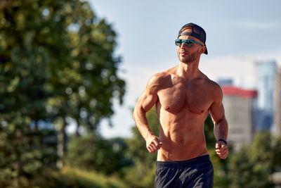 Rear view of shirtless man standing against trees