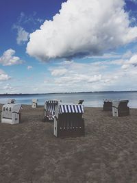 Hooded chairs at beach against cloudy sky