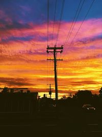 Low angle view of silhouette electricity pylon against dramatic sky during sunset