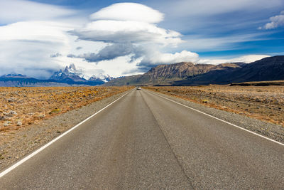 Empty road leading towards mountains against sky