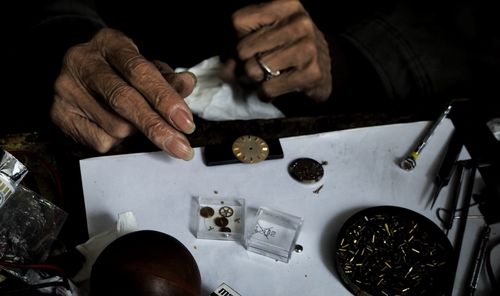 Cropped image of wrinkled hands repairing watch at table