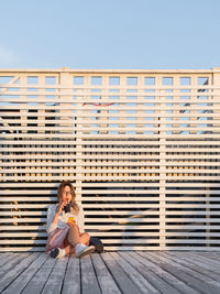 Woman with cup of coffee meets sunset on wooden pier. female listens to music from smartphone. 