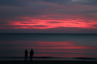 Silhouette couple on beach against cloudy sky during sunset