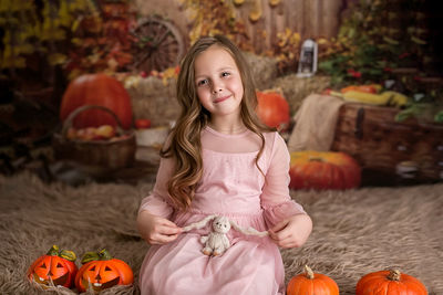 A girl in a pink dress is sitting with a toy rabbit, holding it by the ears. autumn background 