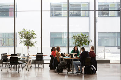 Full length of students talking while sitting at table in university