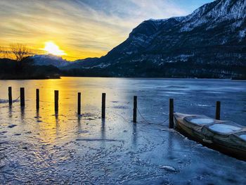Wooden posts in lake against mountains during sunset