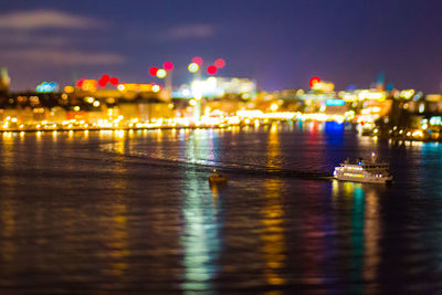 Illuminated city by river against sky at night