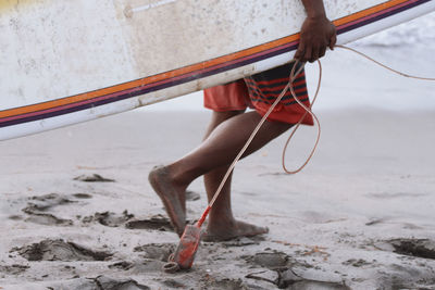 Low section of surfer carrying surfboard at beach