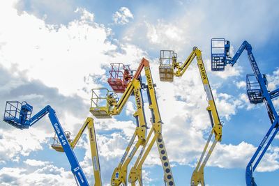 Low angle view of cherry pickers against cloudy sky