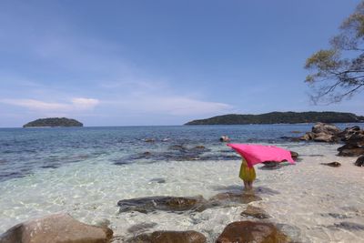 Rear view of woman holding pink sarong in sea against sky