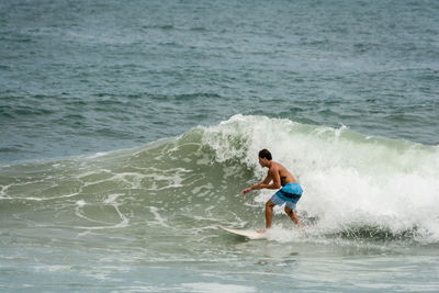Full length of shirtless man surfing in sea