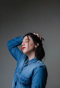 Thoughtful young woman with hand in hair standing against gray background