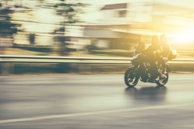 Blurred motion of people riding motor cycle on road