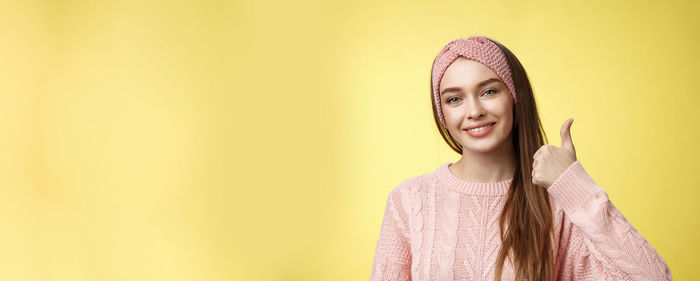 Portrait of young woman standing against yellow wall