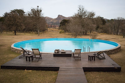 Empty chairs and table by swimming pool against sky