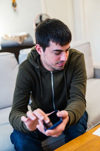 Male with eyesight disability scrolling mobile phone while sitting on couch at home