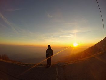 Rear view of man standing on road against sunset sky