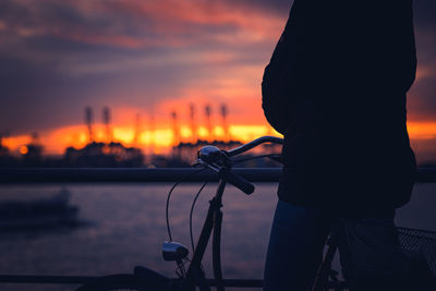 Silhouette man riding bicycle against sky during sunset