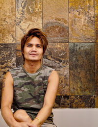 Portrait of young man sitting against wall