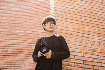 Young man standing against brick wall