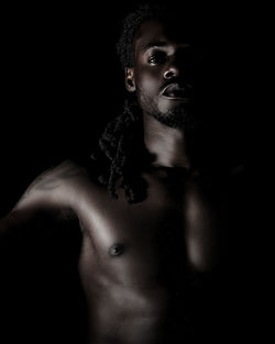 Portrait of shirtless man looking away over black background