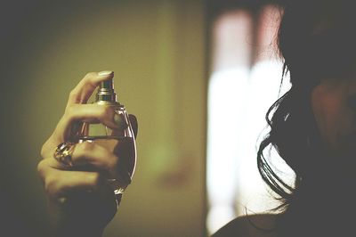 Close-up of woman spraying perfume sitting against wall at home