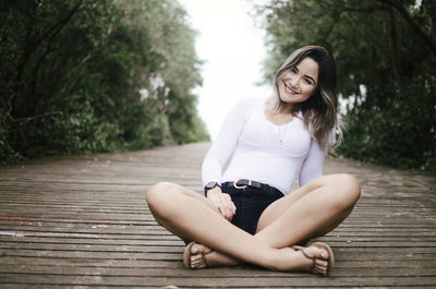 Portrait of smiling young woman sitting on floorboard against plants