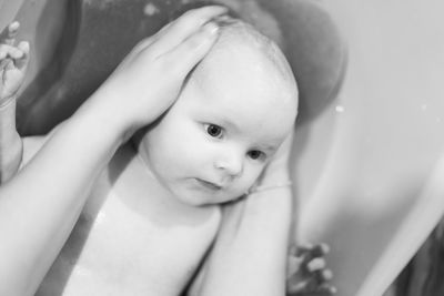 Cropped image of mother giving bath to baby boy in bathtub