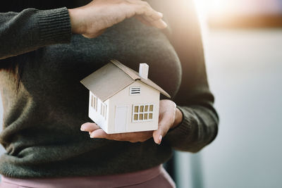 Cropped hand of woman holding model house and gift box