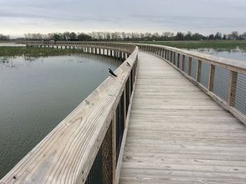 Wooden footbridge over lake against sky