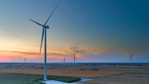 Wind turbines on land against sky during sunset