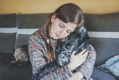 Woman with eyes closed embracing dog at home