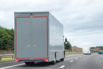 Vehicles on road against cloudy sky