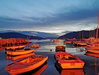 Boats moored at harbor against sky during sunrise