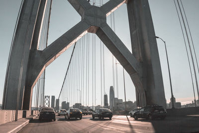 Cars on suspension bridge against sky in city