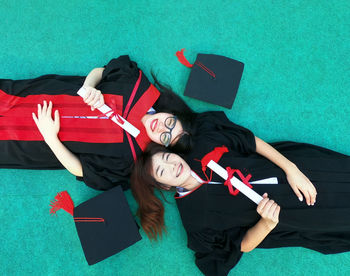 Portrait of friends in graduation gowns lying on floor