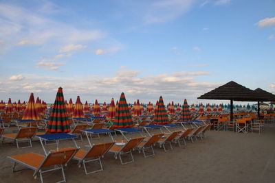 Empty chairs on beach against sky