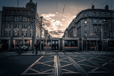 People on street amidst buildings in city at sunset