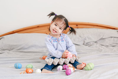 Happy easter. asian chinese baby girl sitting on bed at home and playing with colorful easter eggs. 