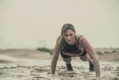 Portrait of young woman crawling on muddy field against sky