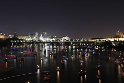 Illuminated city by river against sky at night