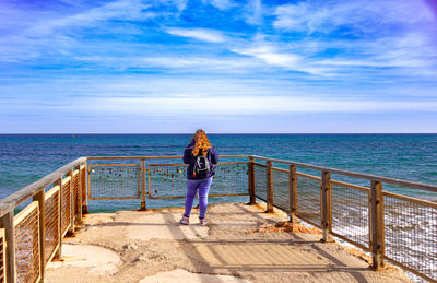 Back view of young woman standing on lookout point watching the horizon in front of the sea.