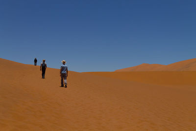 People walking on desert against clear sky
