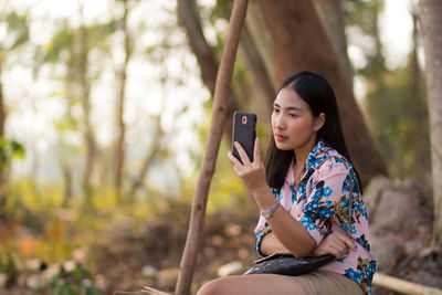 Young woman using mobile phone while sitting on tree