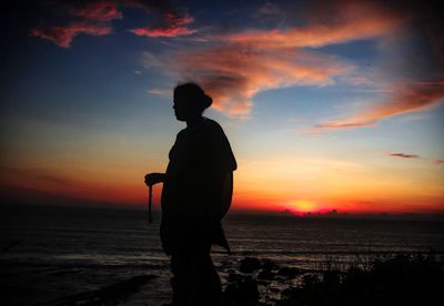 Silhouette man looking at sea against sky during sunset